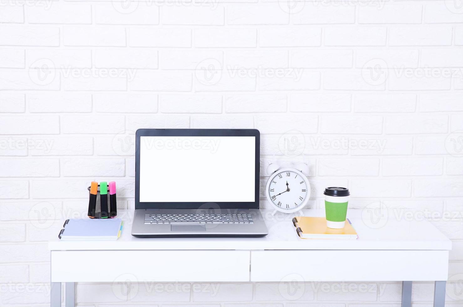 accesorios educativos en la mesa cerca de la pared de ladrillo. computadora vacía y pantalla móvil con lugar para texto. foto