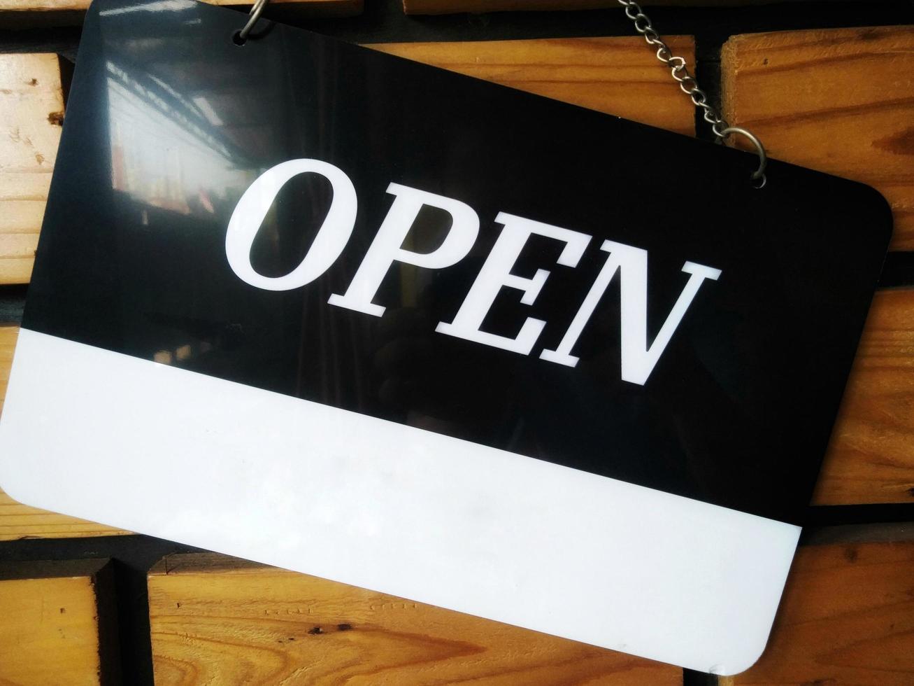 Open signboard black and white color with a symbol that means Shop is open. Hanging on a wooden wall. photo