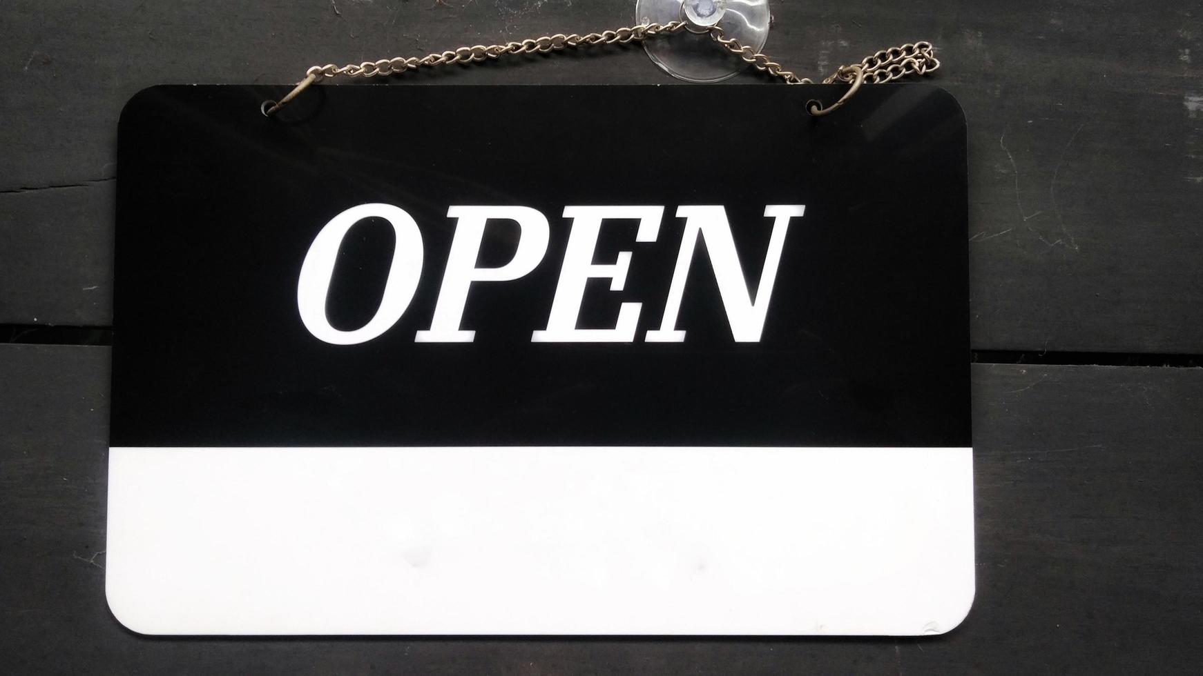 Open signboard black and white color with a symbol that means Shop is open. Hanging on a wooden wall. photo