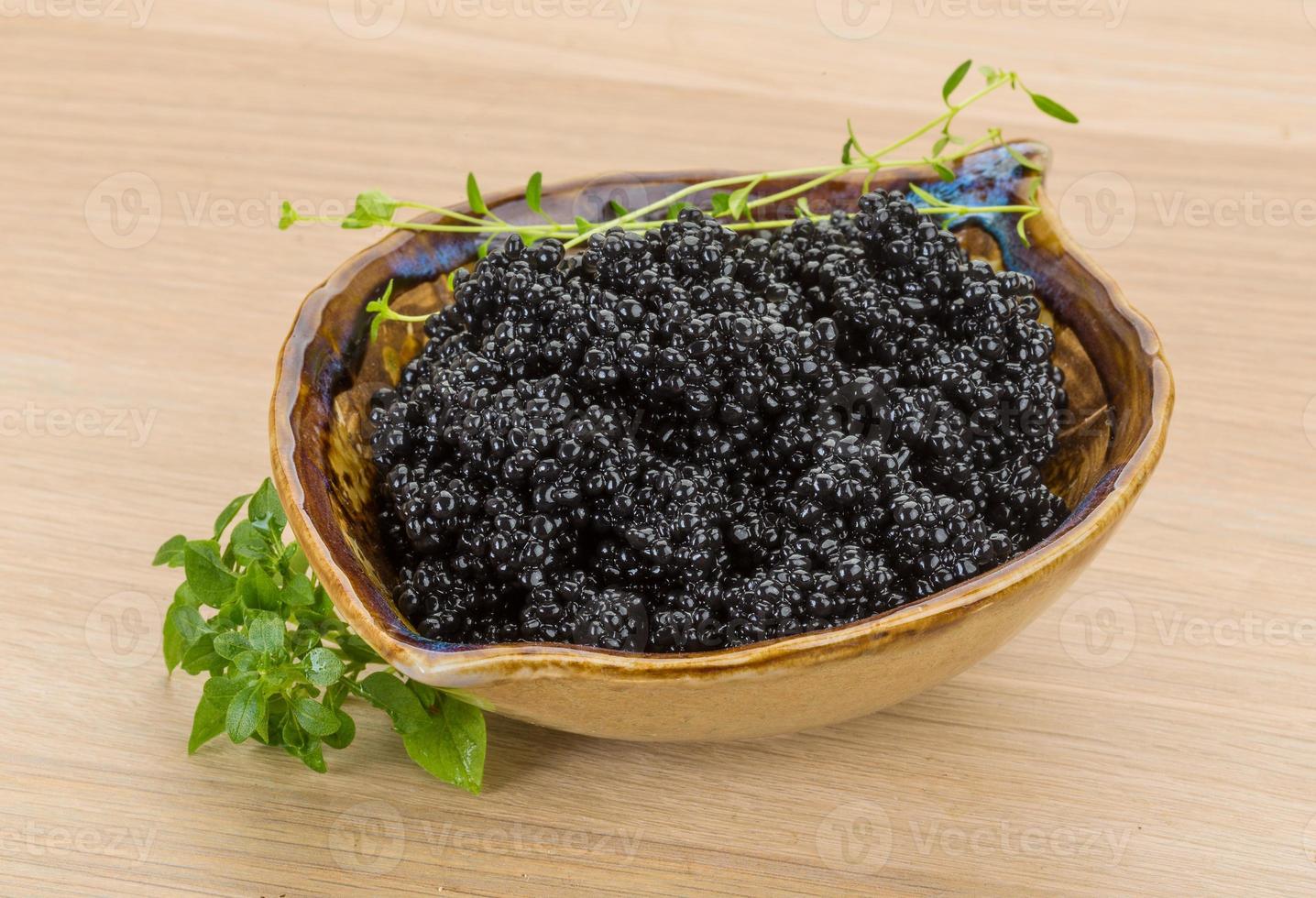 Black caviar in a bowl on wooden background photo