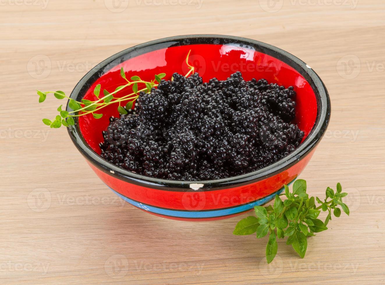 Black caviar in a bowl on wooden background photo