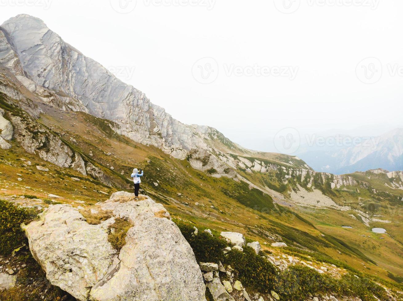 Tourist woman on mountains viewpoint take photo of scenery in Racha, Georgian region. Udziro lake hiking trail