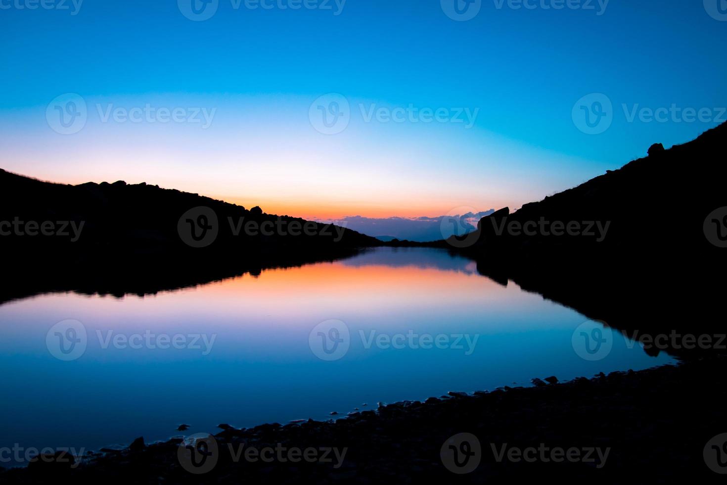 Blue mountain lake in blue hour wit orange after sunset light autumn time. Wild nature and rural mount valley photo