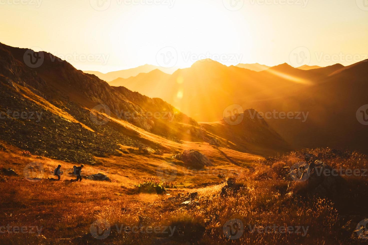 Man and woman hikers in distance hike on trail outdoors on beautiful sunset in autumn together against sun. Cinematic inspirational active people on trek in caucasus mountains photo