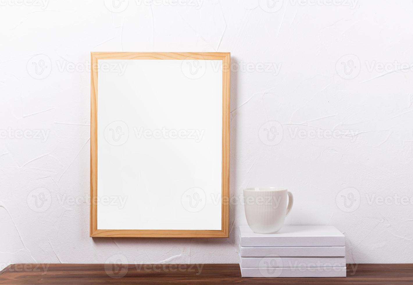 White frame mockup hanging on the wall with stack of books and coffee cup photo