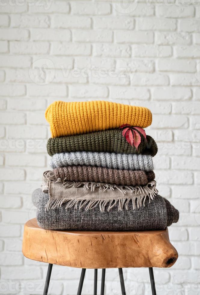 Stack of autumn warm sweaters on modern coffee table, white brick wall background photo
