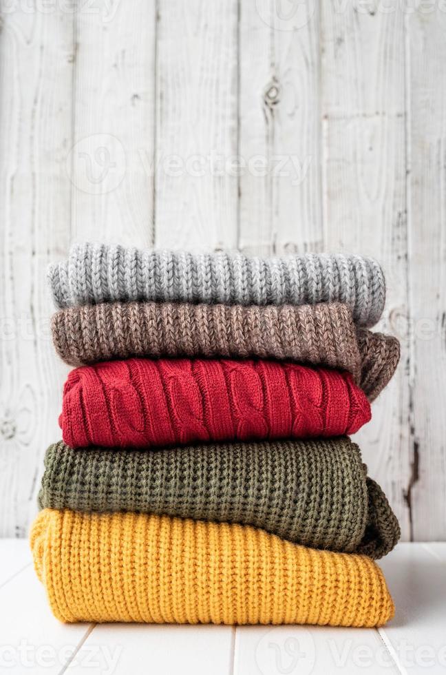 Stack of autumn warm sweaters on white wooden background photo