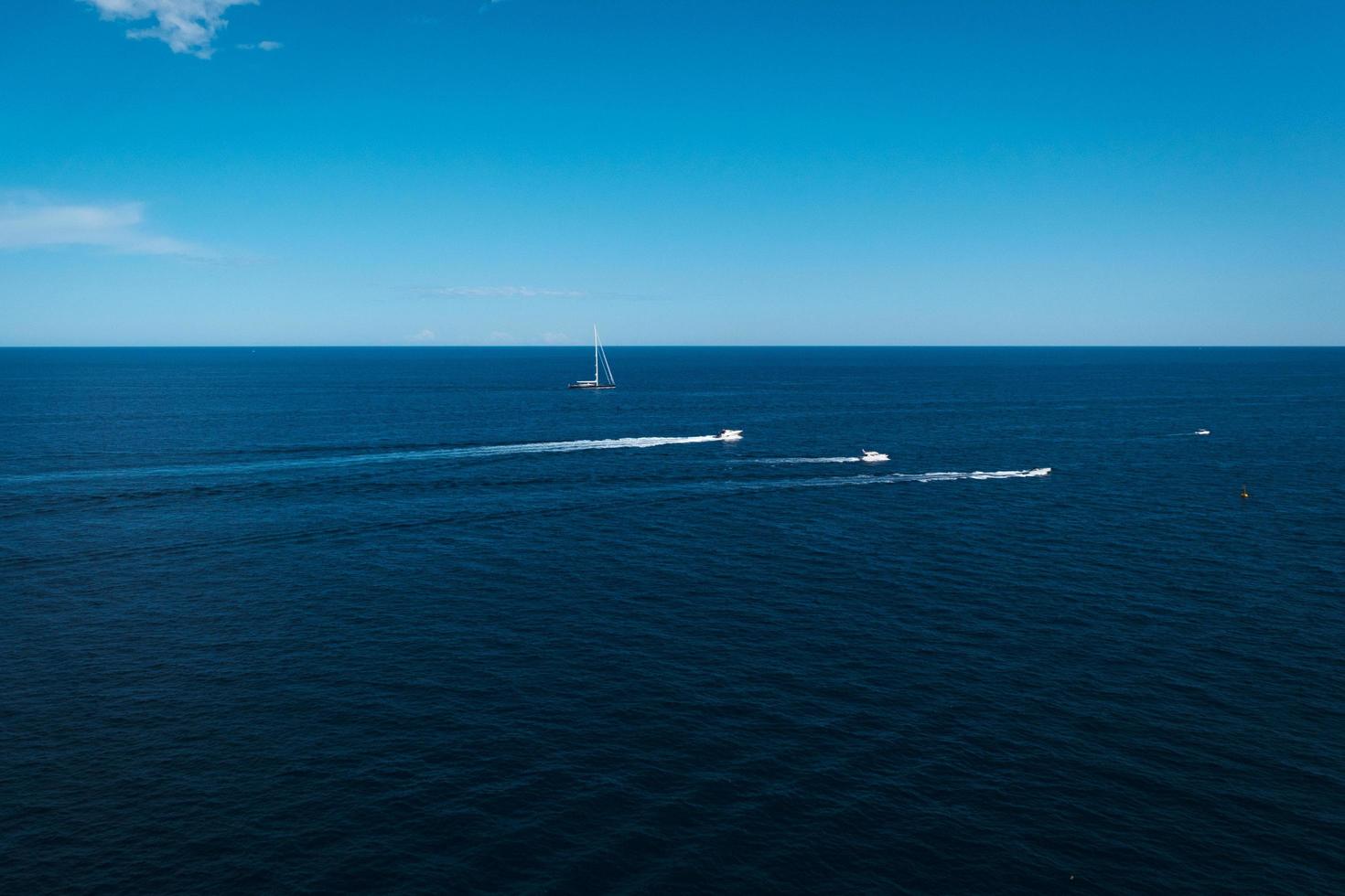pequeños veleros y barcos a motor viajan a través del horizonte azul del mar, fondo, pequeños yates y los barcos navegan sobre las olas del océano profundo, el paisaje marino, los viajes y la aventura. foto