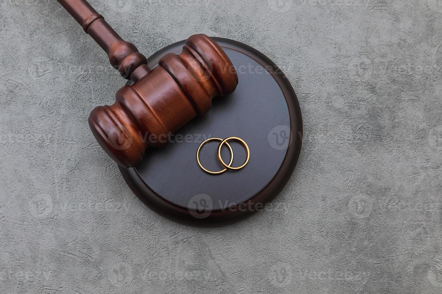 Law theme. Judge gavel wedding rings on concrete stone grey background. Divorce proceedings. Mallet of judge deciding on marriage divorce, marital agreement, legalities of divorce. photo