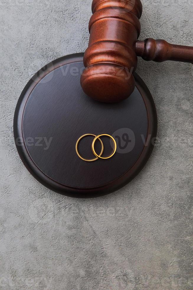 Law theme. Judge gavel wedding rings on concrete stone grey background. Divorce proceedings. Mallet of judge deciding on marriage divorce, marital agreement, legalities of divorce. photo