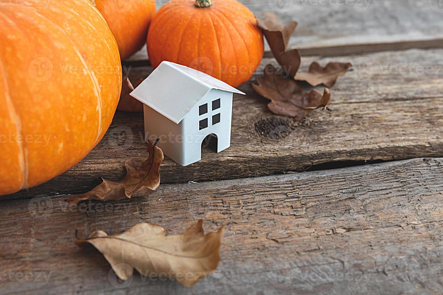 Autumnal Background. Toy house and pumpkin on wooden background. Thanksgiving banner copy space. Hygge mood, change of seasons concept. Hello Autumn with family Halloween party. photo