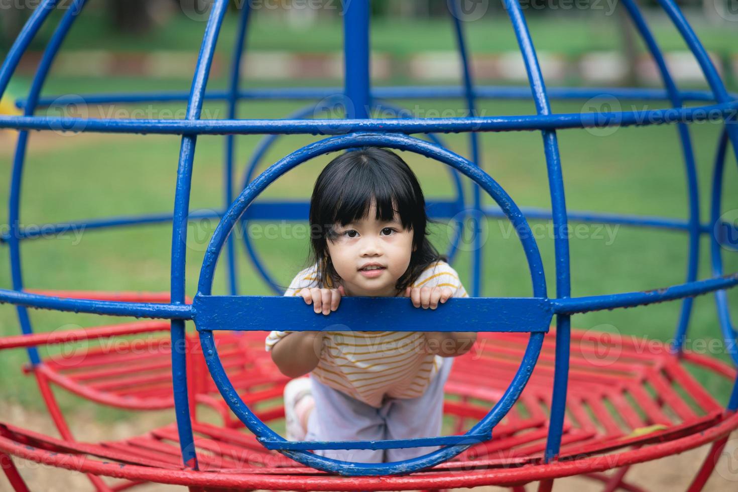 Cute asian girl smile and play on school or kindergarten yard or playground. Healthy summer activity for children. Little asian girl climbing outdoors at playground. photo
