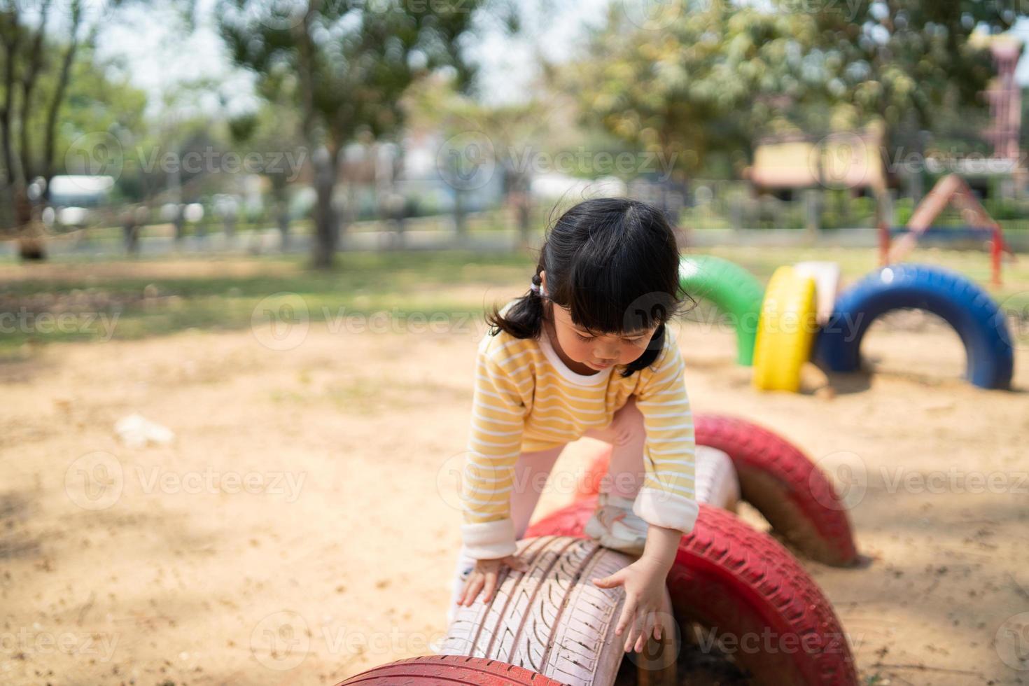 linda niña asiática sonríe jugar en la escuela o en el jardín de infantes o en el patio de recreo. Actividad de verano saludable para niños. niña asiática escalando al aire libre en el patio de recreo. niño jugando en el patio de recreo al aire libre. foto