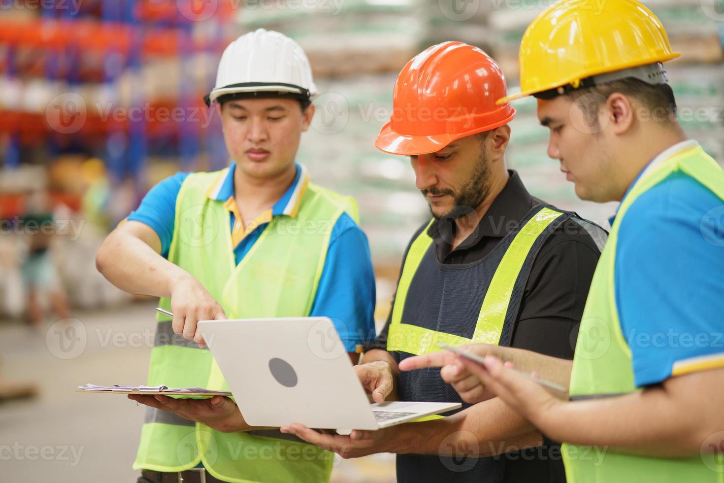 Manager man using laptop check stock and co-worker point finger to laptop at warehouse. Worker wearing high visibility clothing and hard hat, helmet to checking count up goods or boxes for delivery. photo