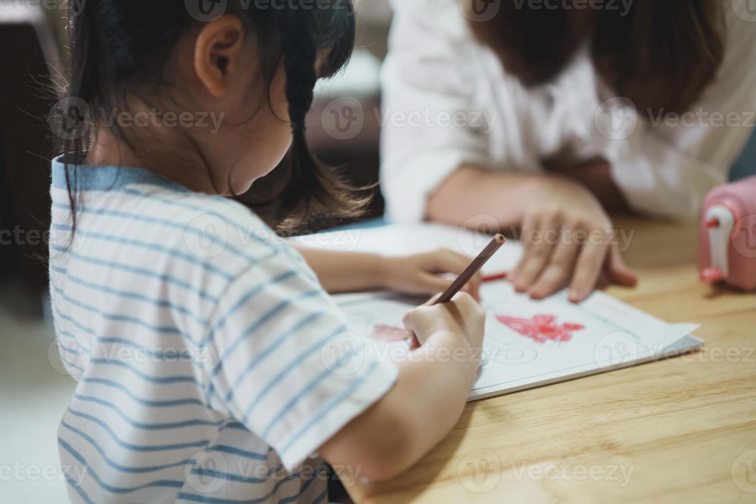 Cute little child painting with colorful paints. Asian girl and mother using crayon drawing color. Daughter and mom doing homework coloring cartoon characters. Baby artist activity lifestyle concept. photo