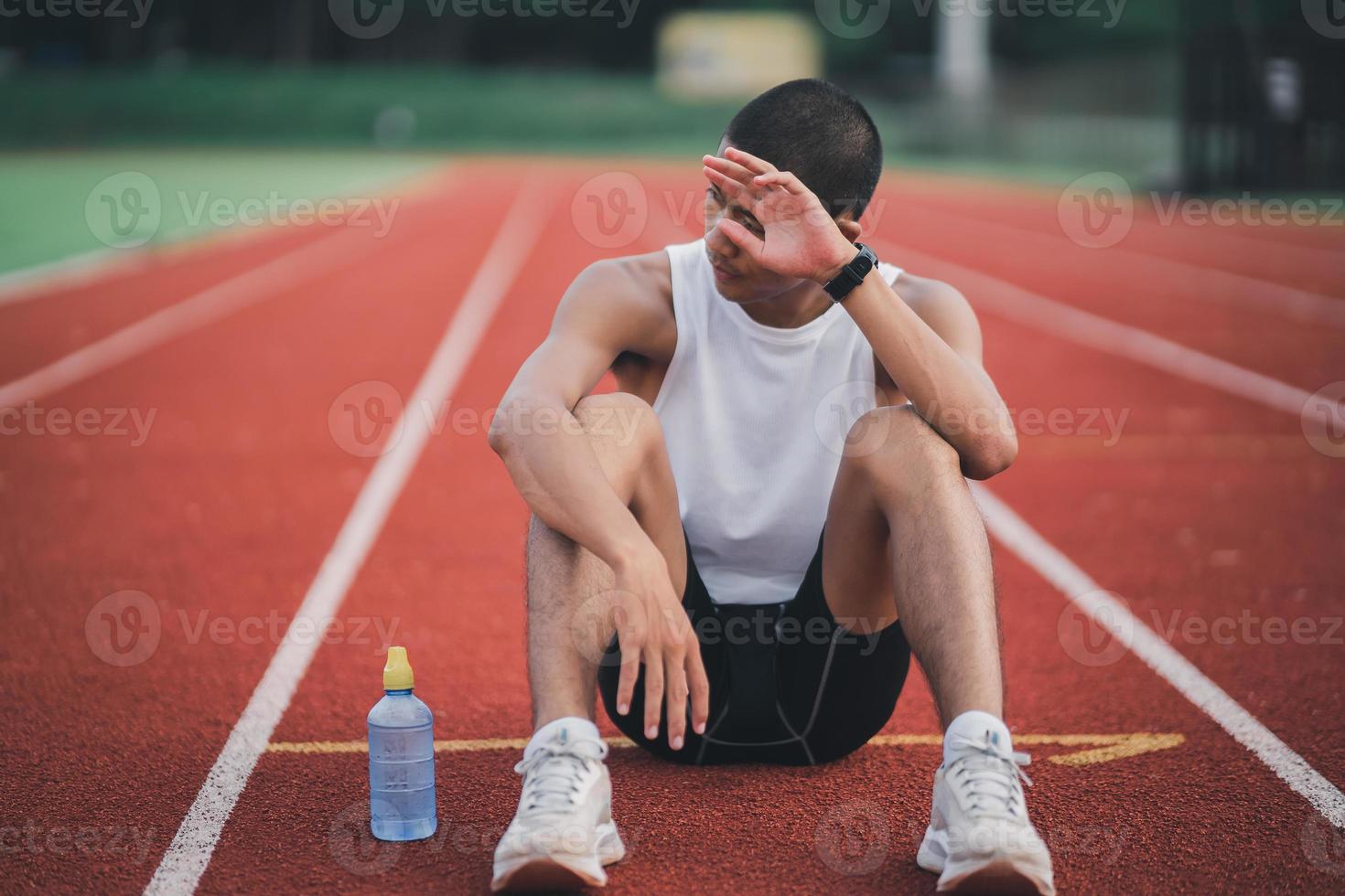 atletas corredor deporte hombre descansando botella agua cansado y sediento practicando en una pista de atletismo en un estadio. correr entrenamiento beber agua. concepto de carrera de hombre deportivo. foto