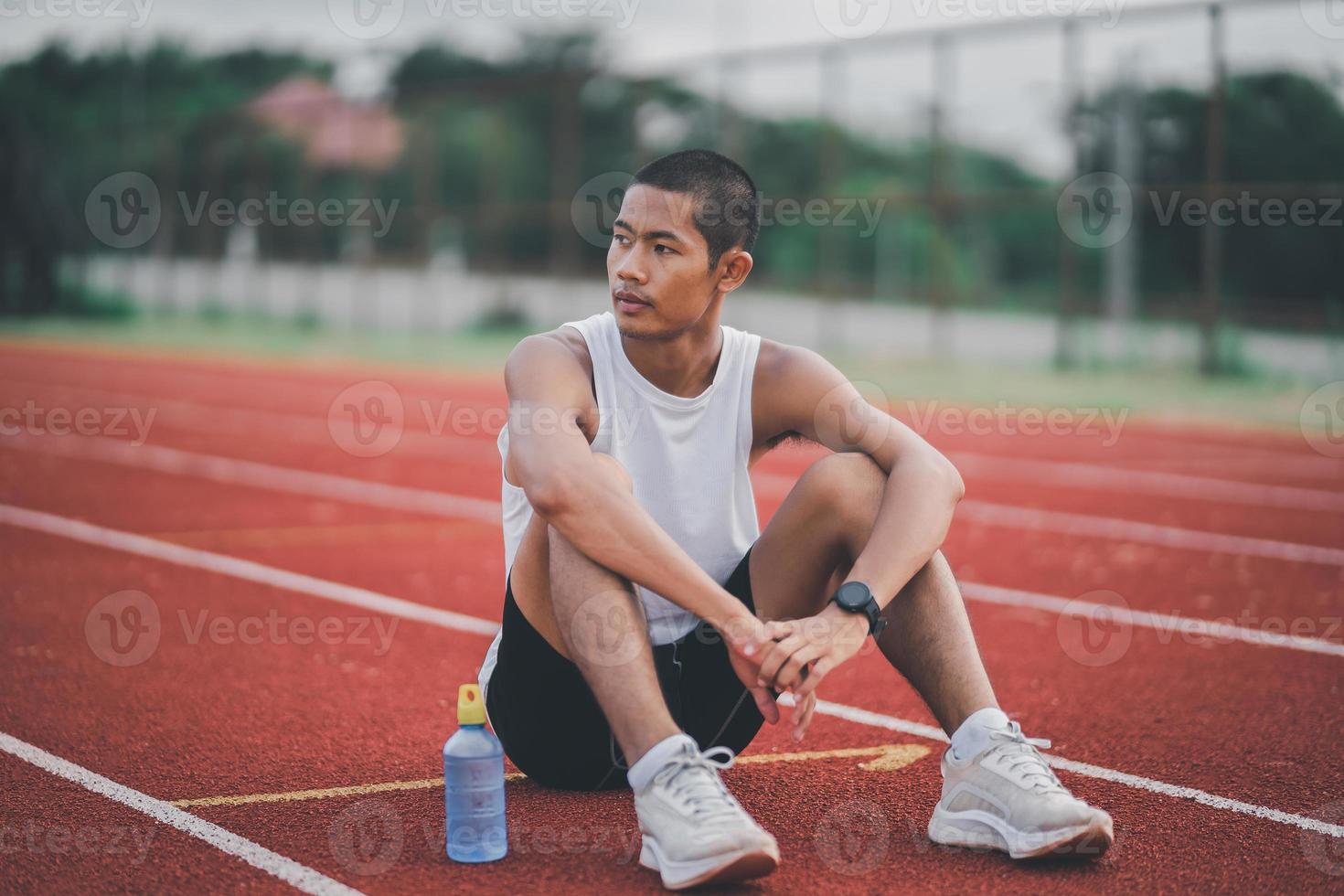 atletas corredor deporte hombre descansando botella agua cansado y sediento practicando en una pista de atletismo en un estadio. correr entrenamiento beber agua. concepto de carrera de hombre deportivo. foto