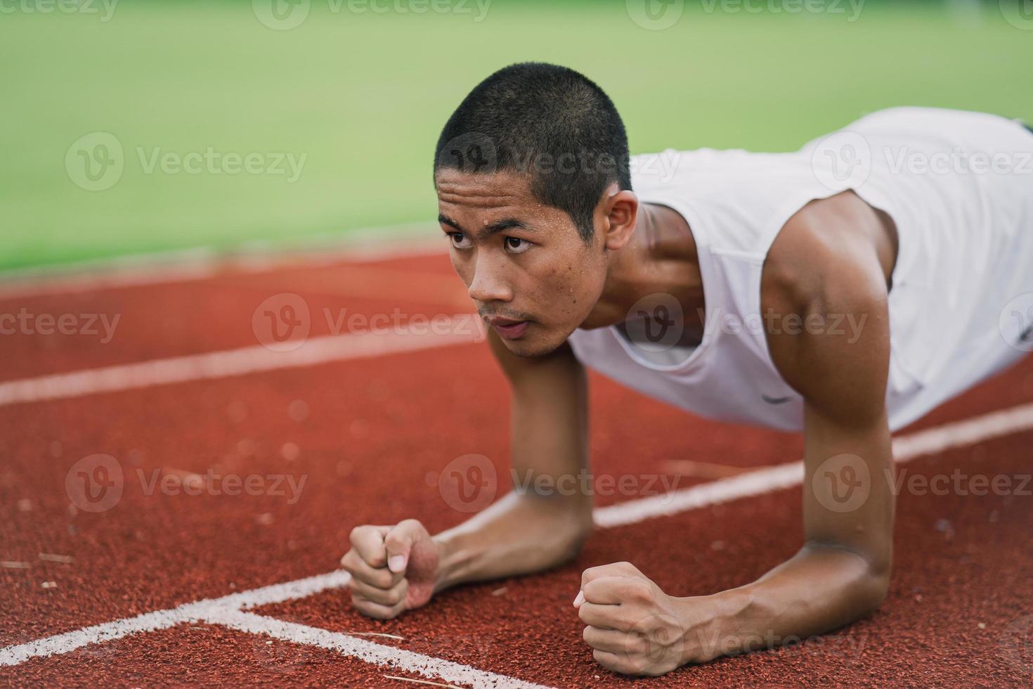 Athletes sport man runner wearing white sportswear to planking stretching and warm up before practicing on a running track at a stadium. Runner sport concept. photo