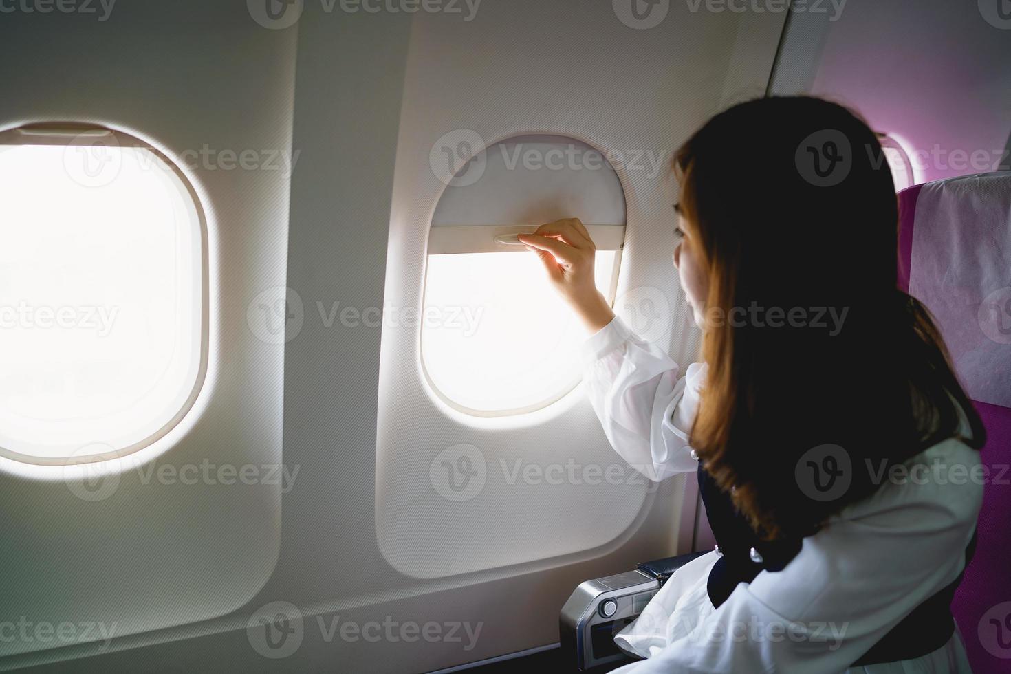 Asian woman sitting in a seat in airplane and looking out the window going on a trip, asian woman passenger is leaving for a trip by plane on vacation. Vacation travel concept. photo