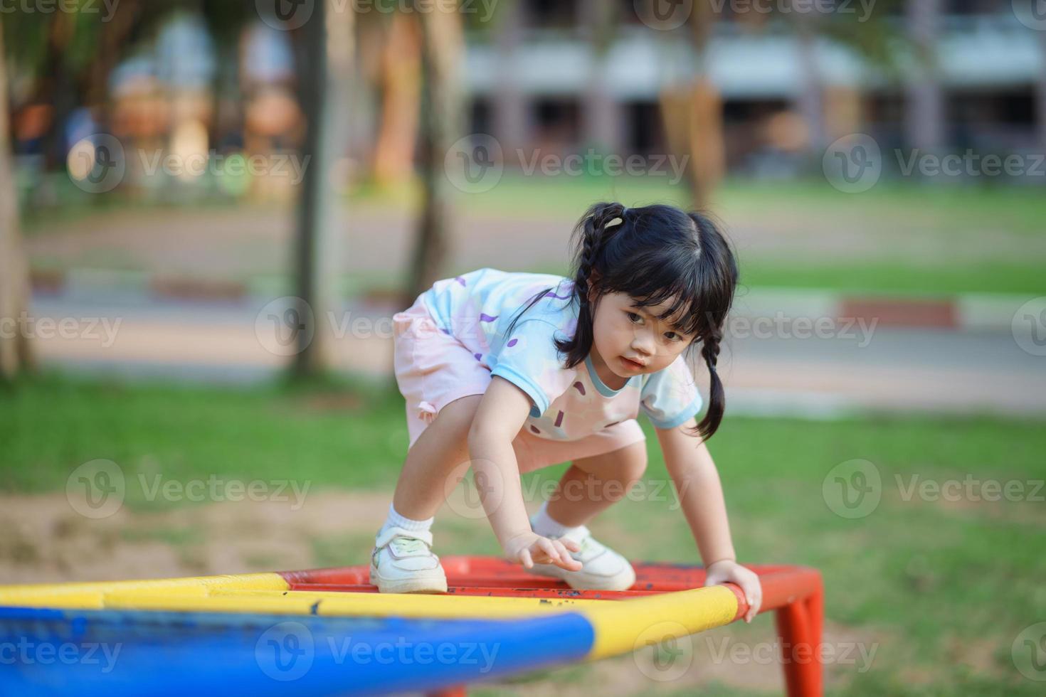 Cute asian girl smile play on school or kindergarten yard or playground. Healthy summer activity for children. Little asian girl climbing outdoors at playground. Child playing on outdoor playground. photo