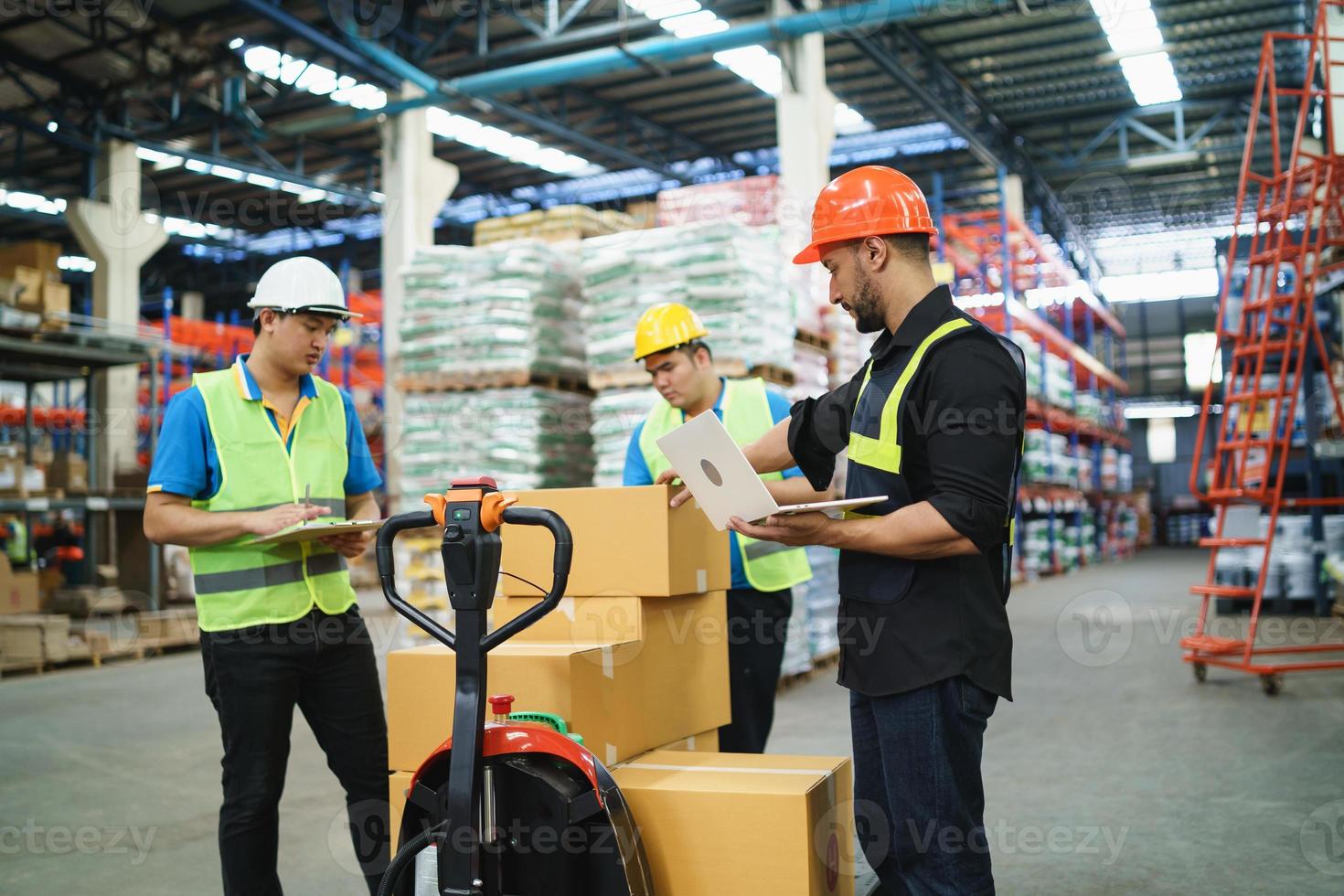 Manager man using laptop check stock cardboard on forklift and co-worker at warehouse. Worker wearing high visibility clothing and hard hat, helmet to checking count up goods or boxes for delivery. photo