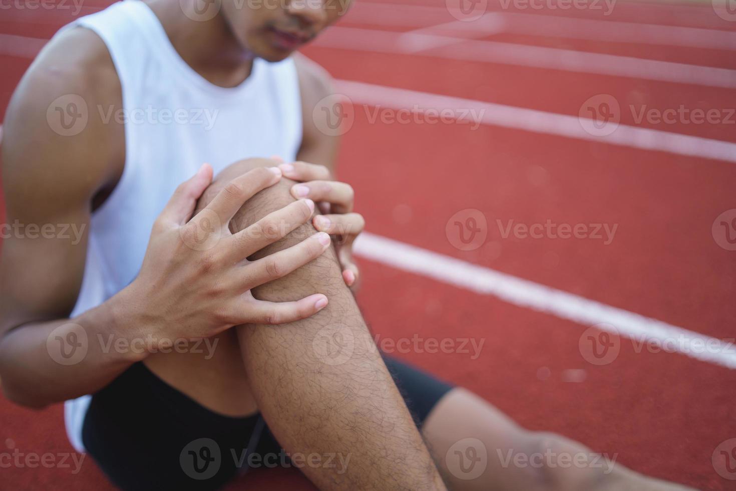 Athletes sport man runner wearing white sportswear to sitting feeling pain in his leg or knee after practicing on a running track at a stadium, copy space. Runner sport injury concept. photo