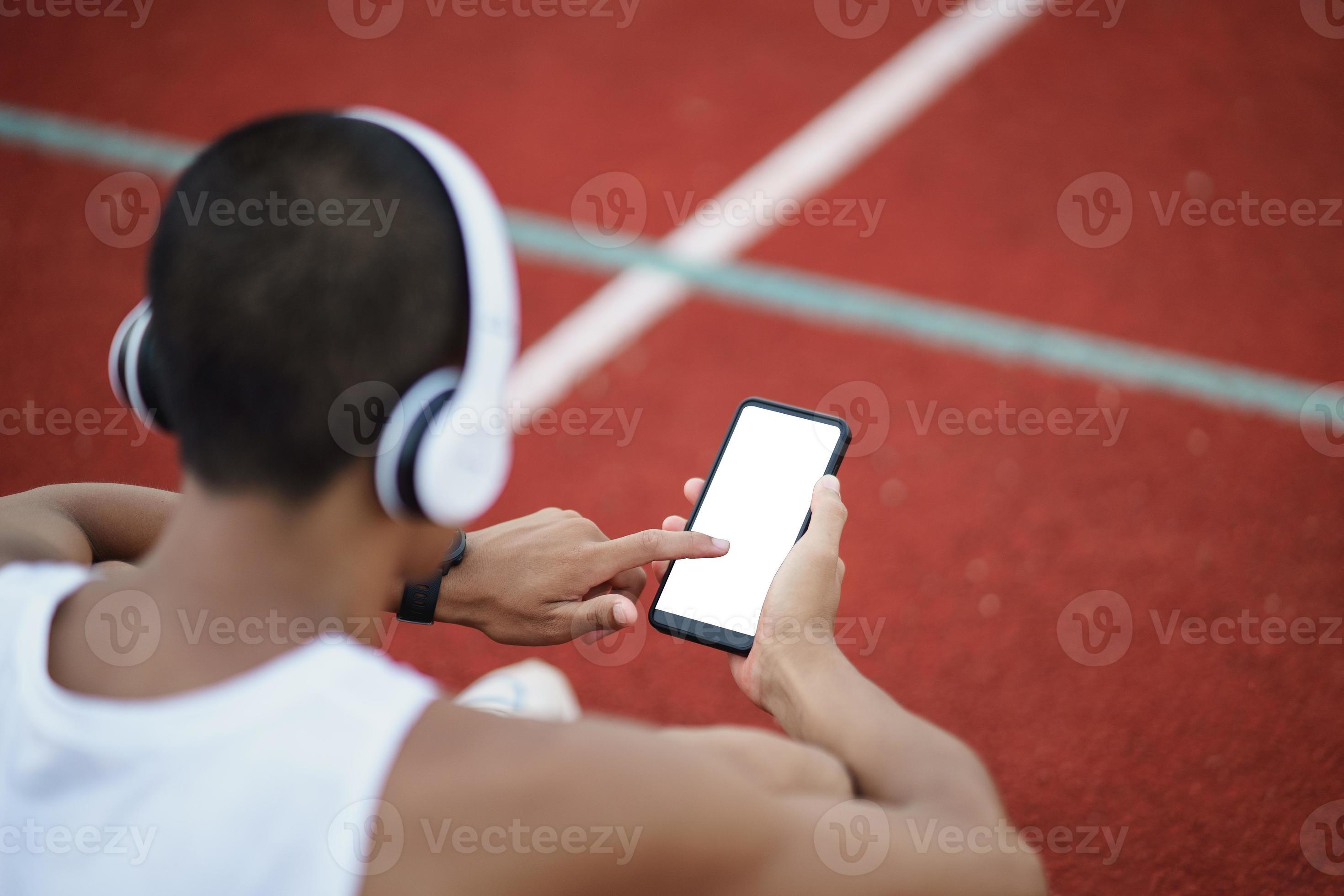 Deportista asiático en forma usando auriculares blancos y usando el  teléfono móvil para escuchar música mientras descansa o antes de correr  haciendo ejercicio en el gimnasio concepto de gimnasio deportivo saludable