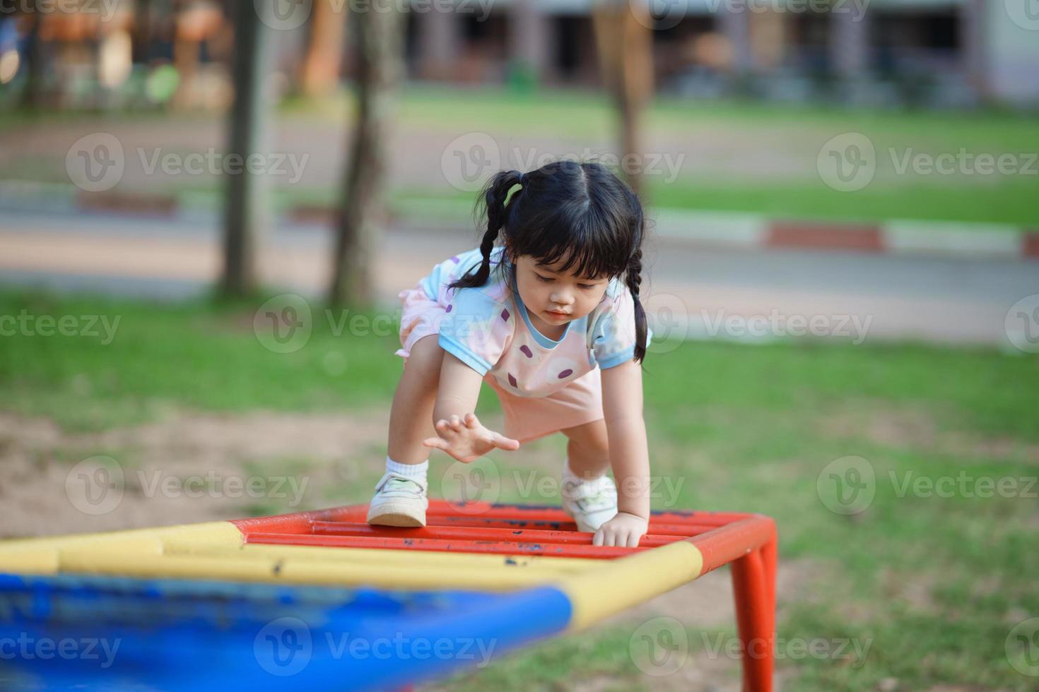 Cute asian girl smile play on school or kindergarten yard or playground. Healthy summer activity for children. Little asian girl climbing outdoors at playground. Child playing on outdoor playground. photo