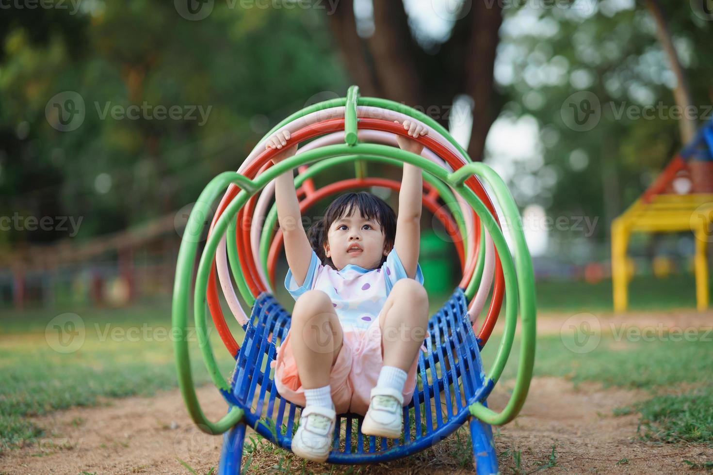 Cute asian girl smile play on school or kindergarten yard or playground. Healthy summer activity for children. Little asian girl climbing outdoors at playground. Child playing on outdoor playground. photo