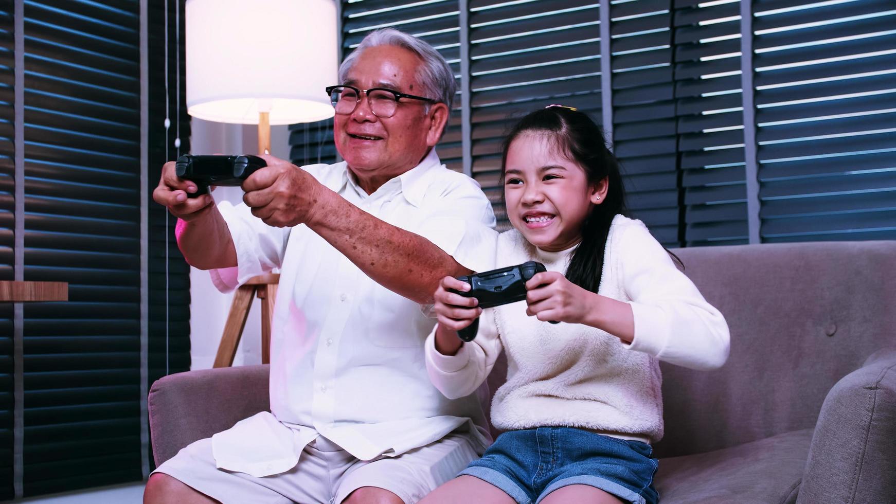 Grandpa and granddaughter are having fun playing video games together in the living room at home. photo