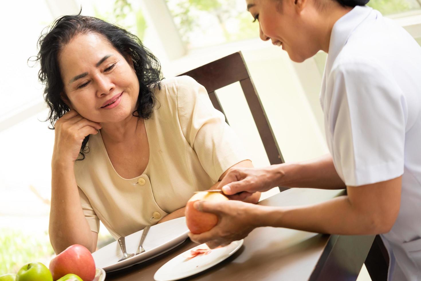Asian nurse peeling apple for adult female patient in the room. photo