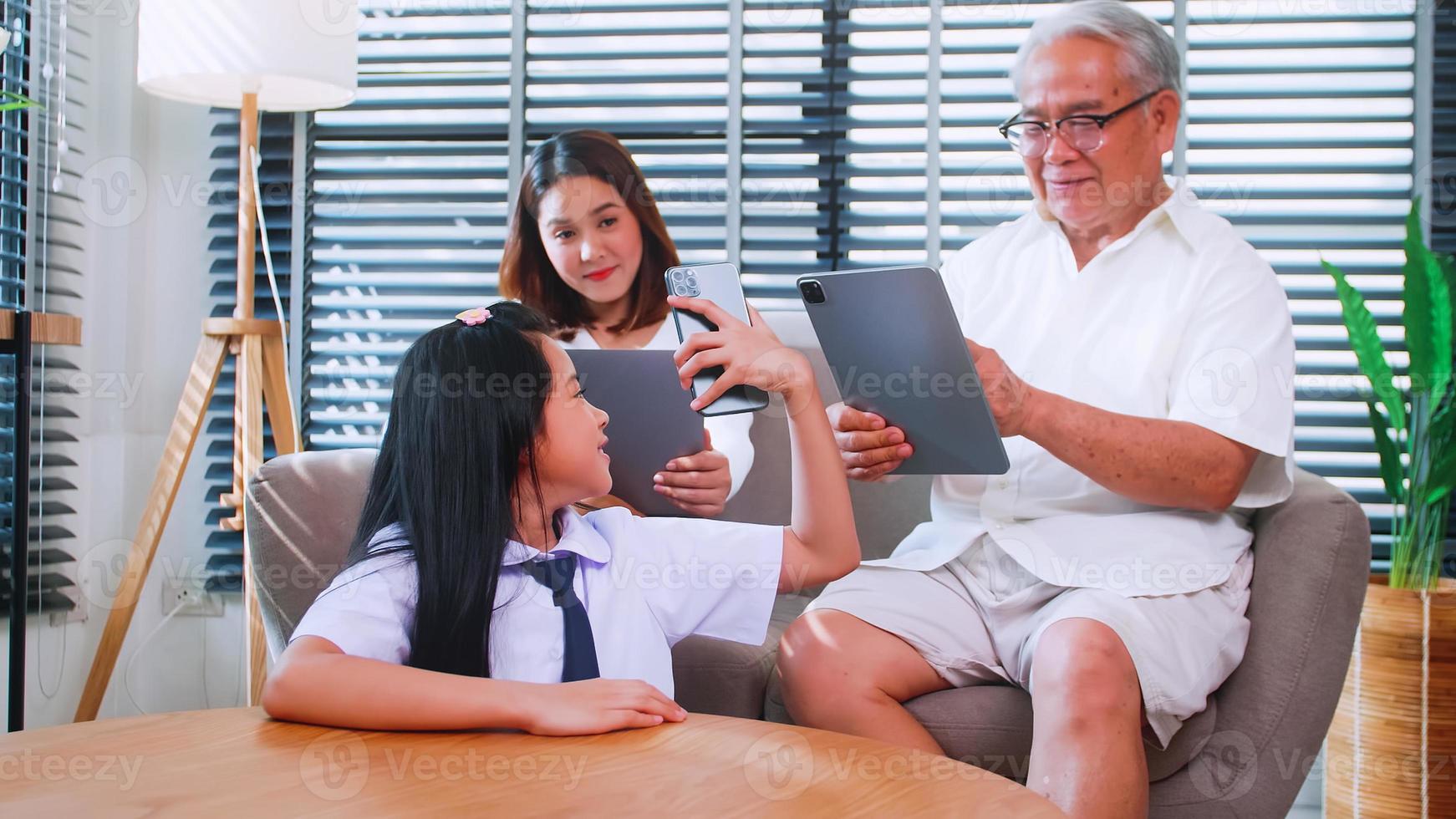 Grandpa, mother and daughter use wireless technology while relaxing in the living room. Asian family is enjoying the modern mobile technology in their home. photo