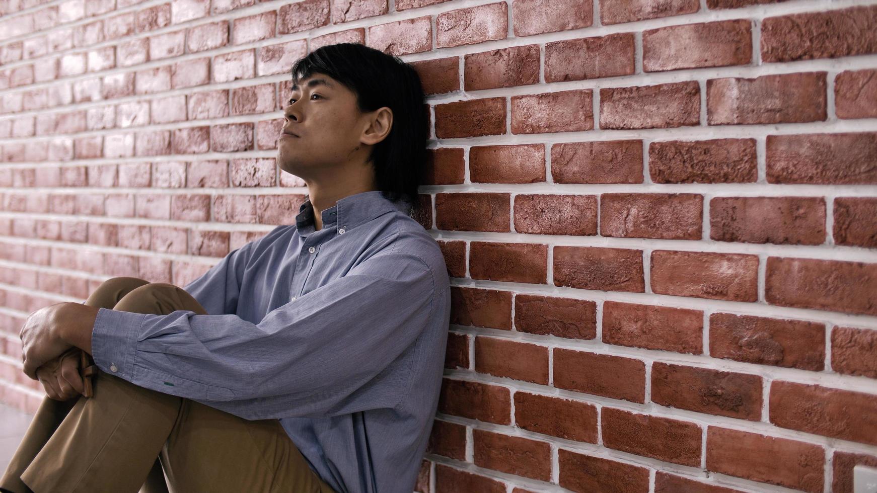 joven deprimido sentado en el suelo contra una pared foto