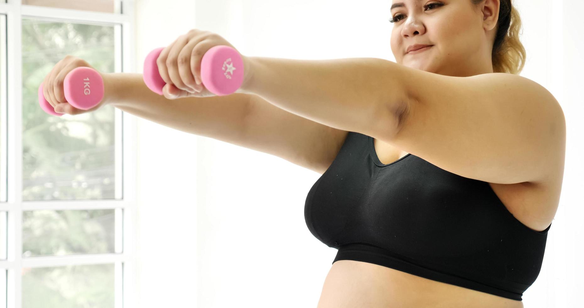 Chubby woman doing exercise by dumbbell in a room. photo