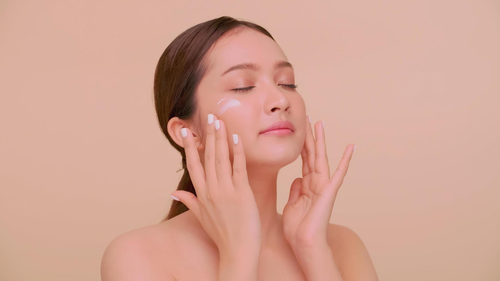 hermoso rostro de mujer joven asiática con piel natural. retrato de una niña aplicando crema humectante en la cara. foto