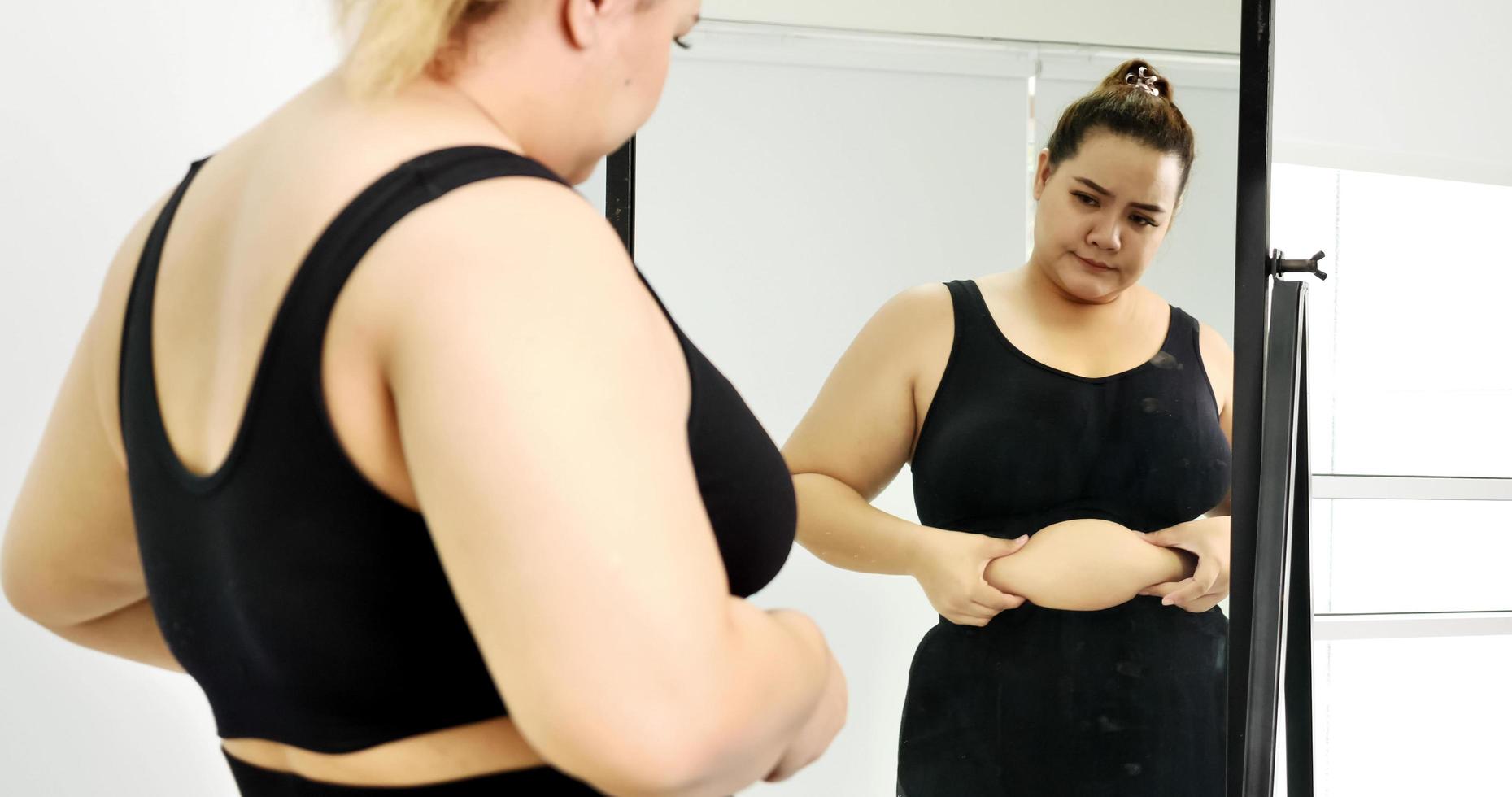 Chubby woman standing and looking at her stomach in a mirror. photo