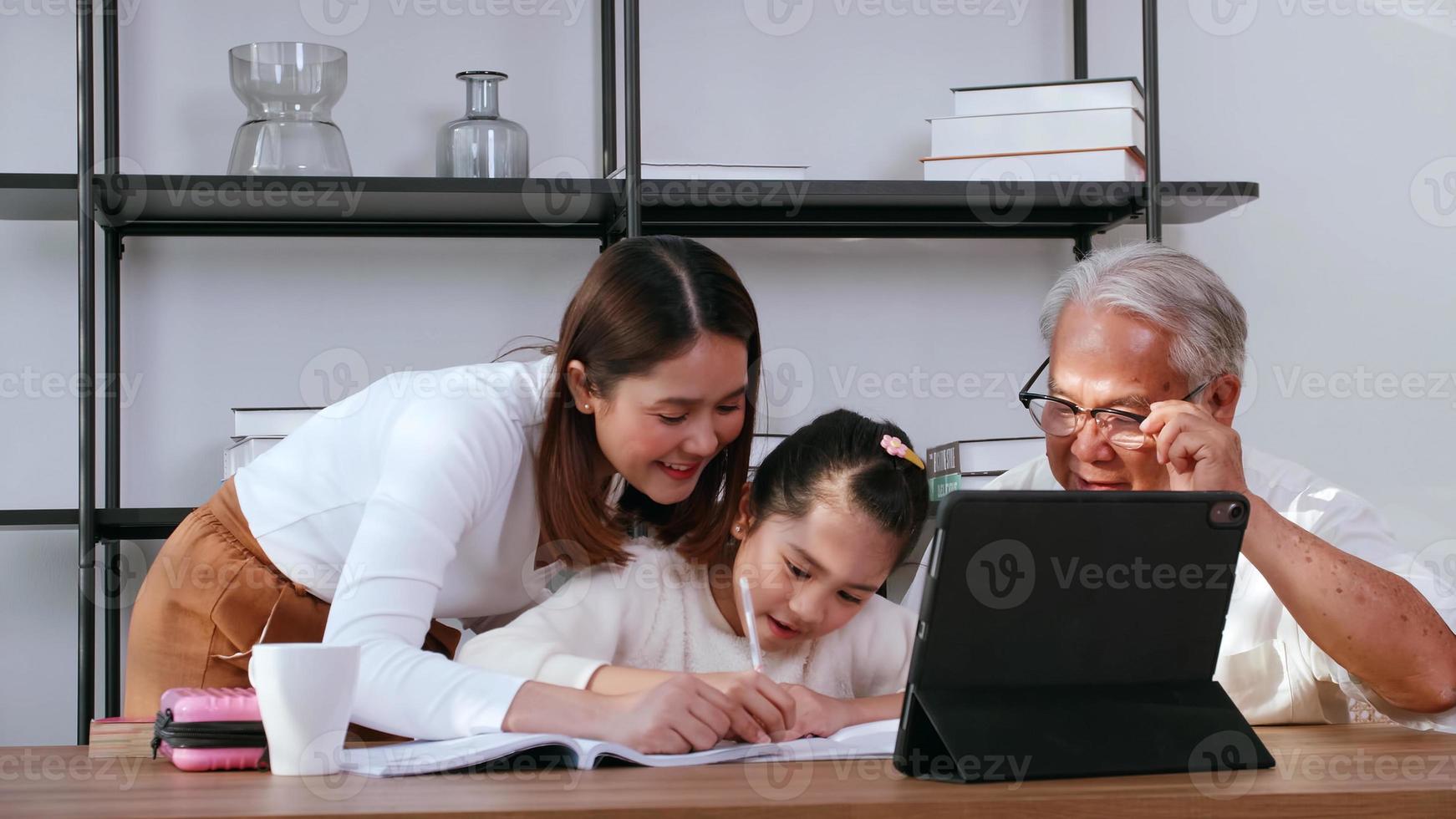 Grandfather and mother are teaching daughter homework while studying online at home. photo