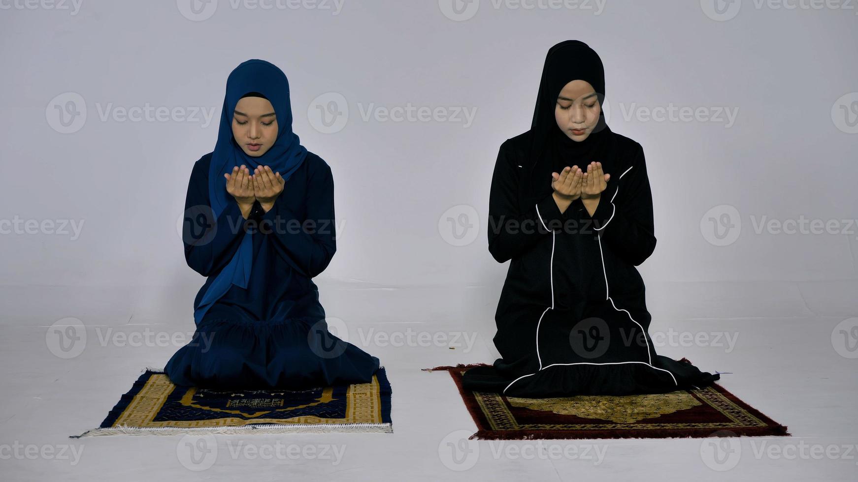 Two Asian Muslim young women in traditional hijab are praying glorify Allah and practicing the Islamic faith in mosque. photo