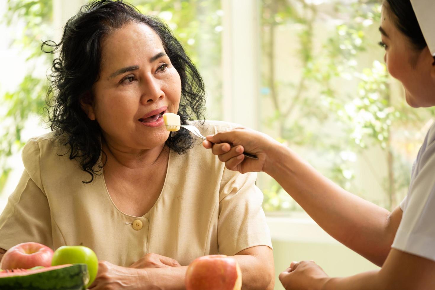 nurse feeding apple to adult female patient in the room. photo