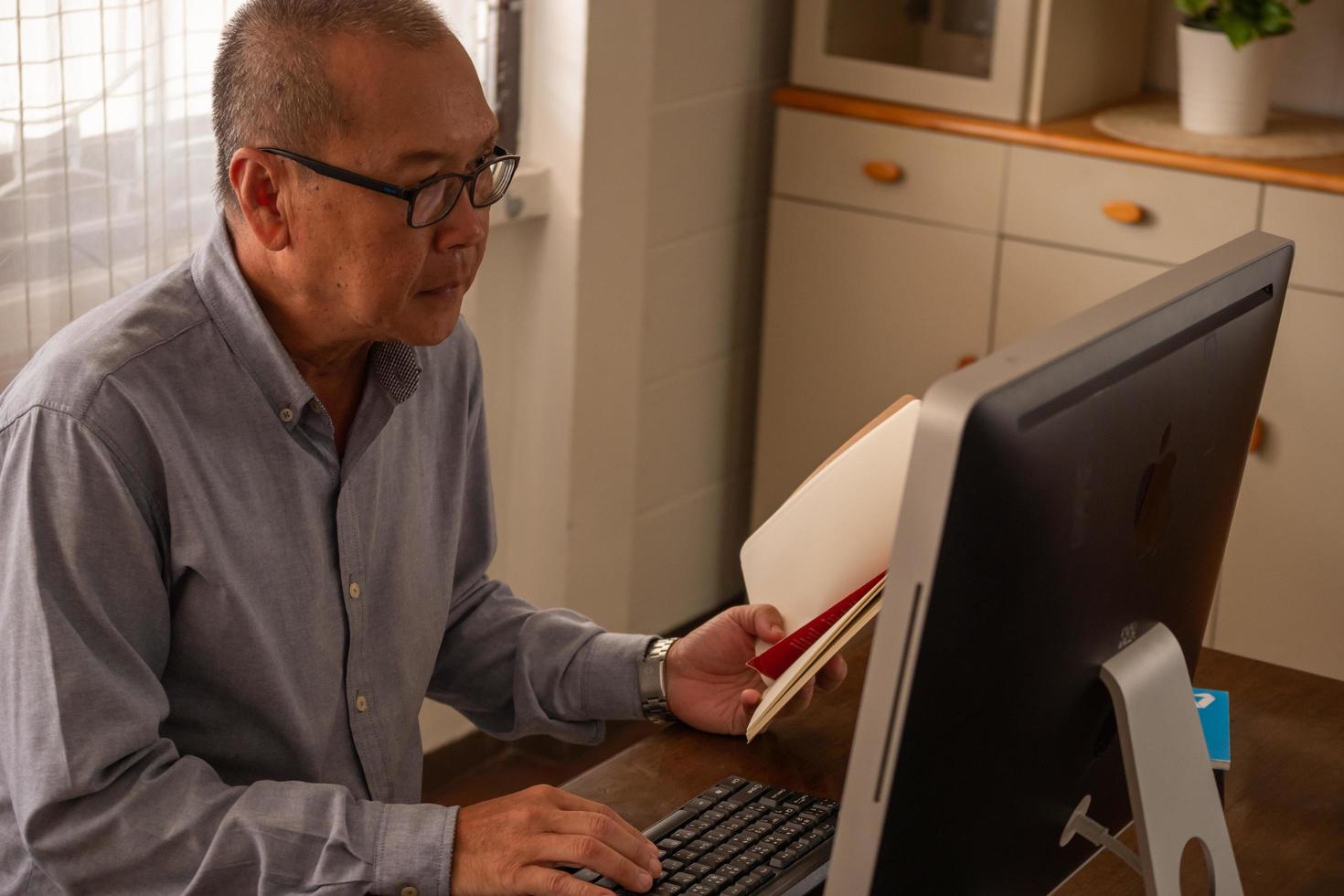 Asian businessman typing on a computer keyboard and holding a book in the office room. photo