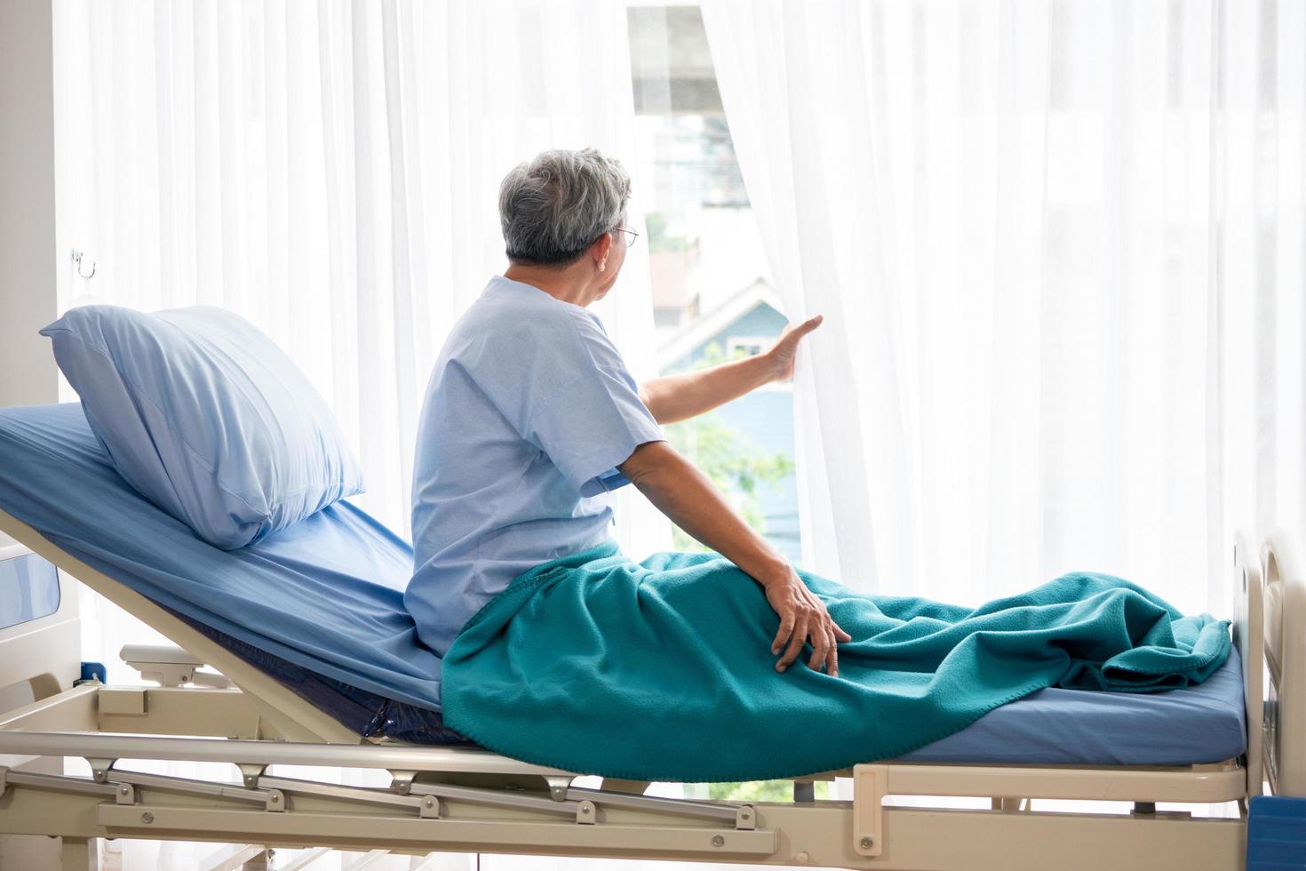 Asian patient man looking outside and sitting on hospital bed in the hospital room. photo