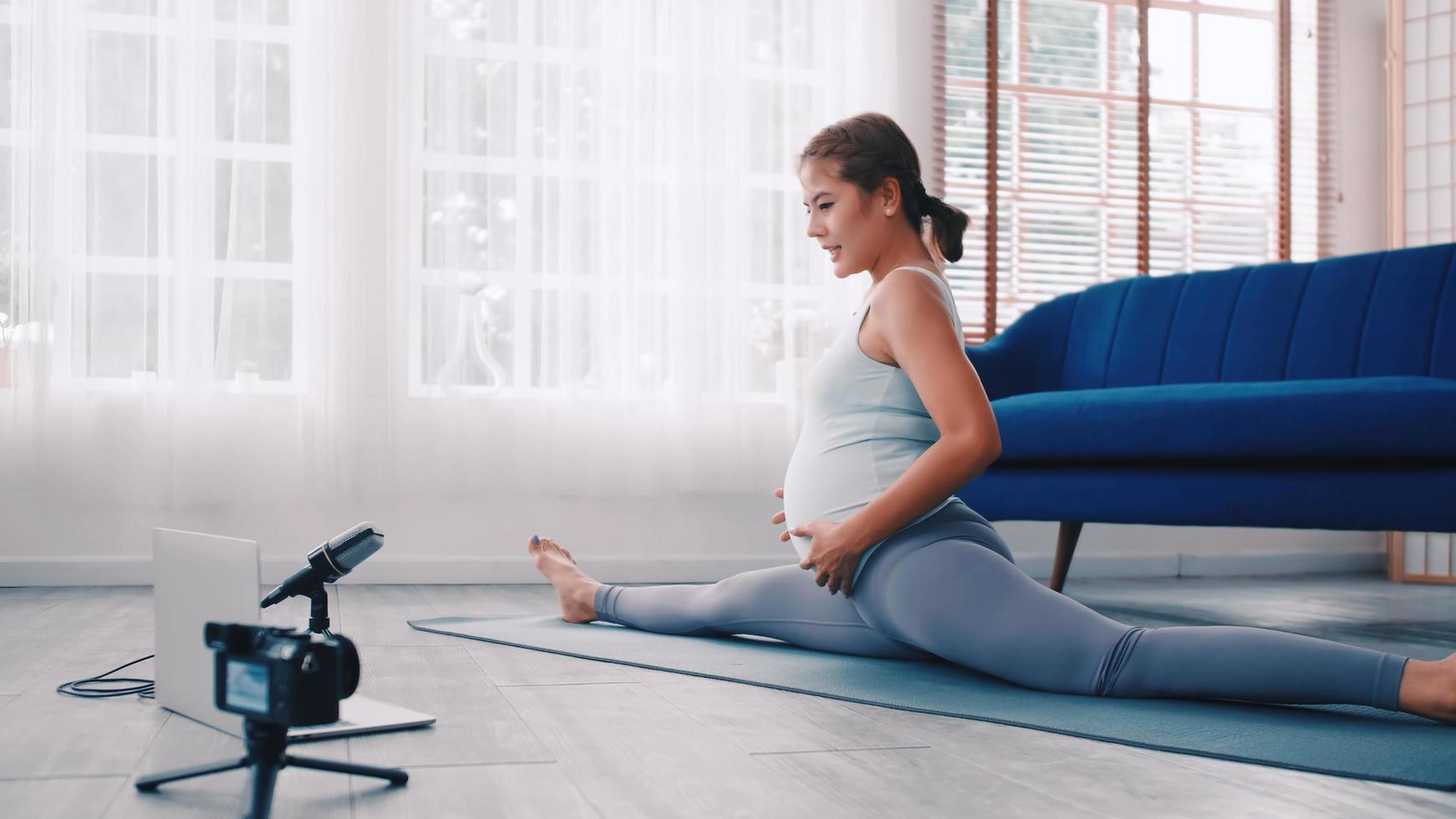 Asian pregnant woman teaching Pilates exercises online at home. photo