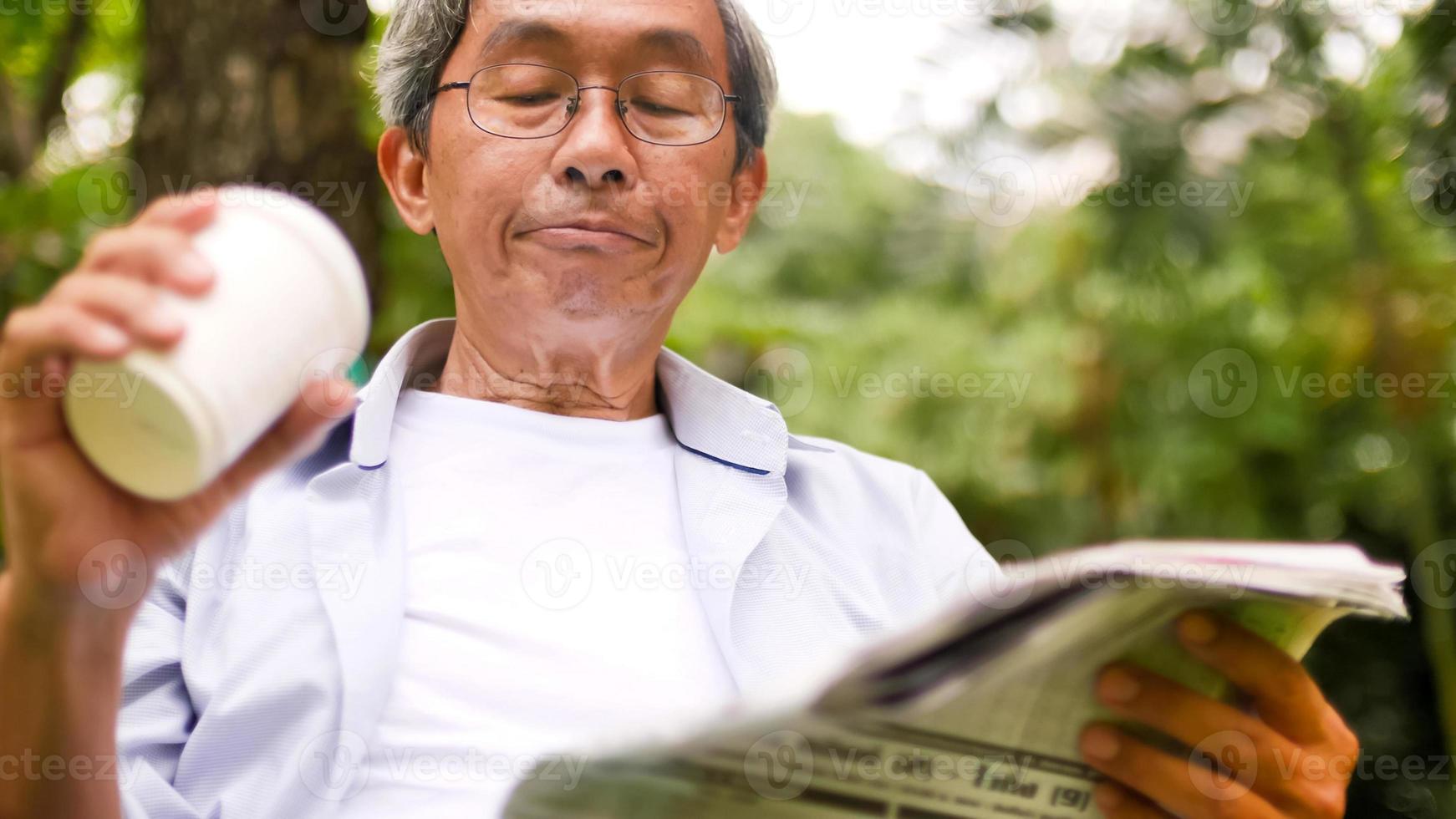 Asian man drinking coffee and reading newspaper at the park. photo