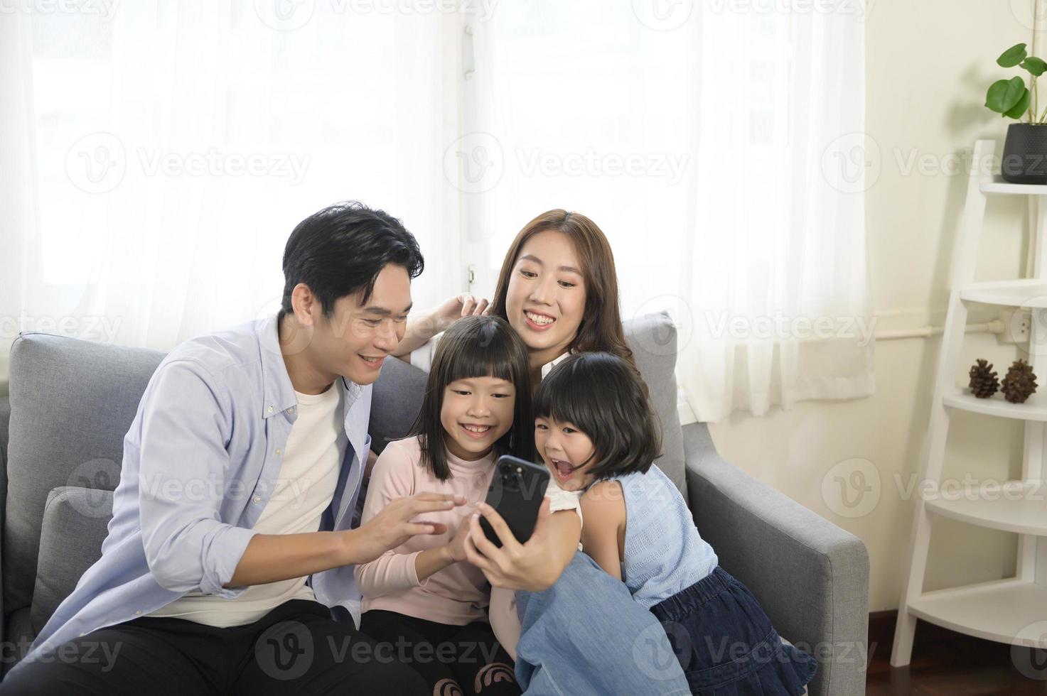 Asian family with children holding smartphone and making video call at home photo