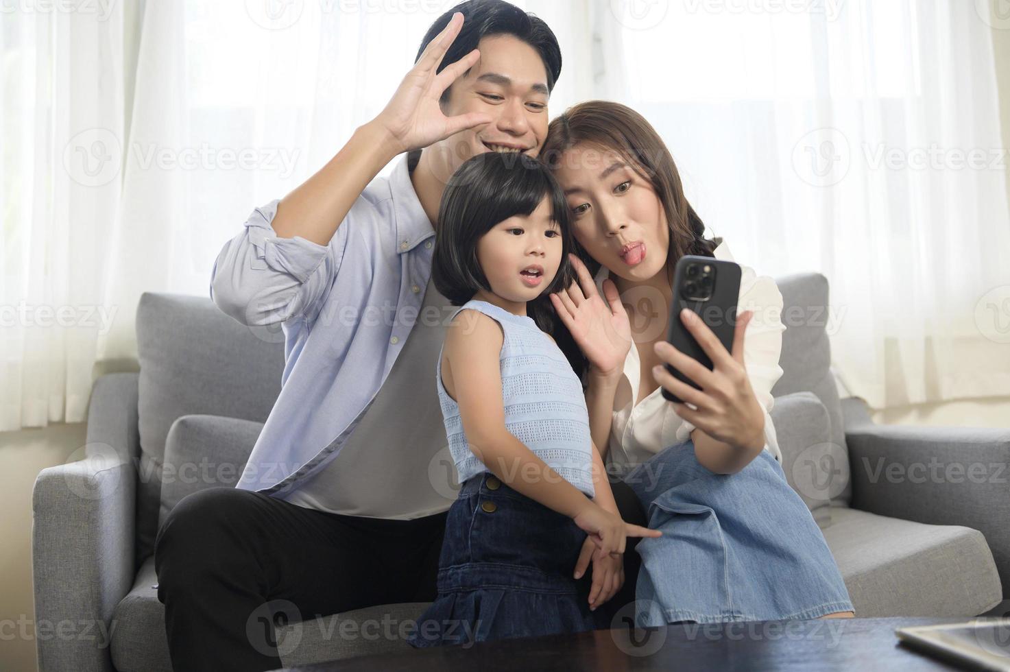 Asian family with children holding smartphone and making video call at home photo