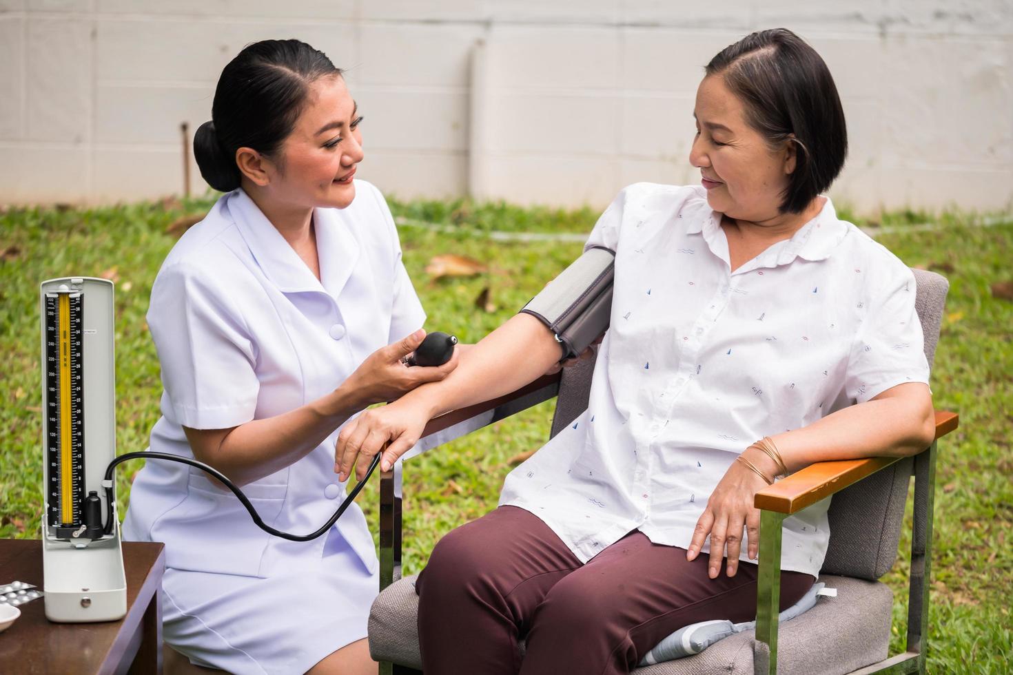 Beautiful nurse doing pressure measuring for female patient at the hospital park. photo