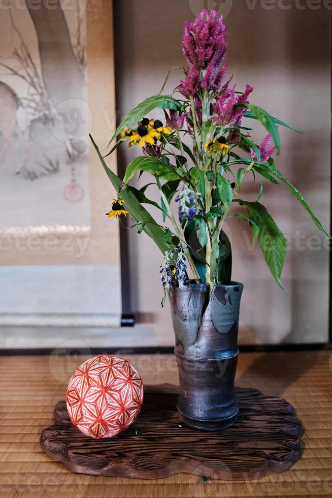 Purple and yellow flowers in vase next to cloth ball in traditional Japanese home photo