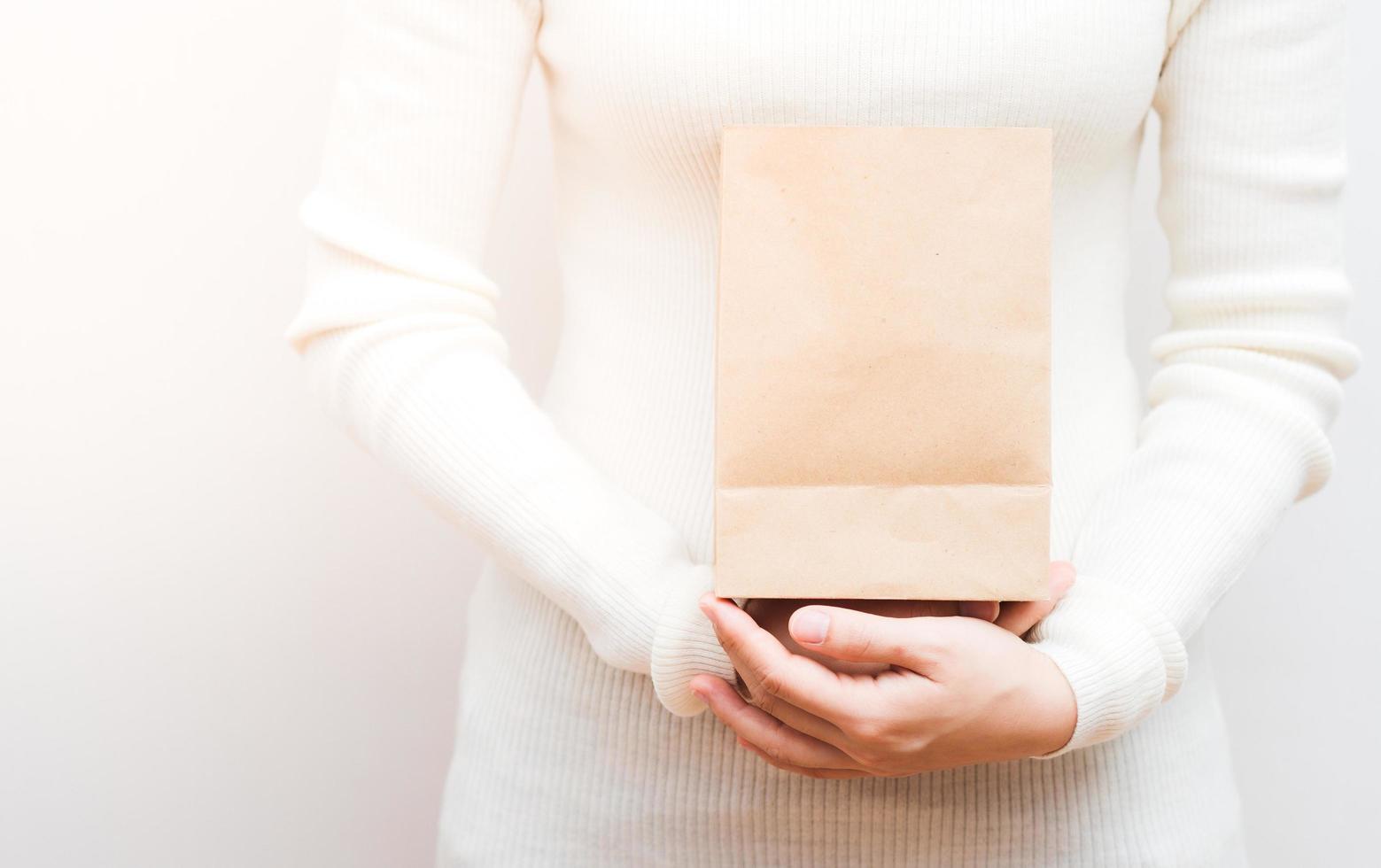 Close up female holds in hand brown clear empty blank craft  eco paper bag on white background. photo