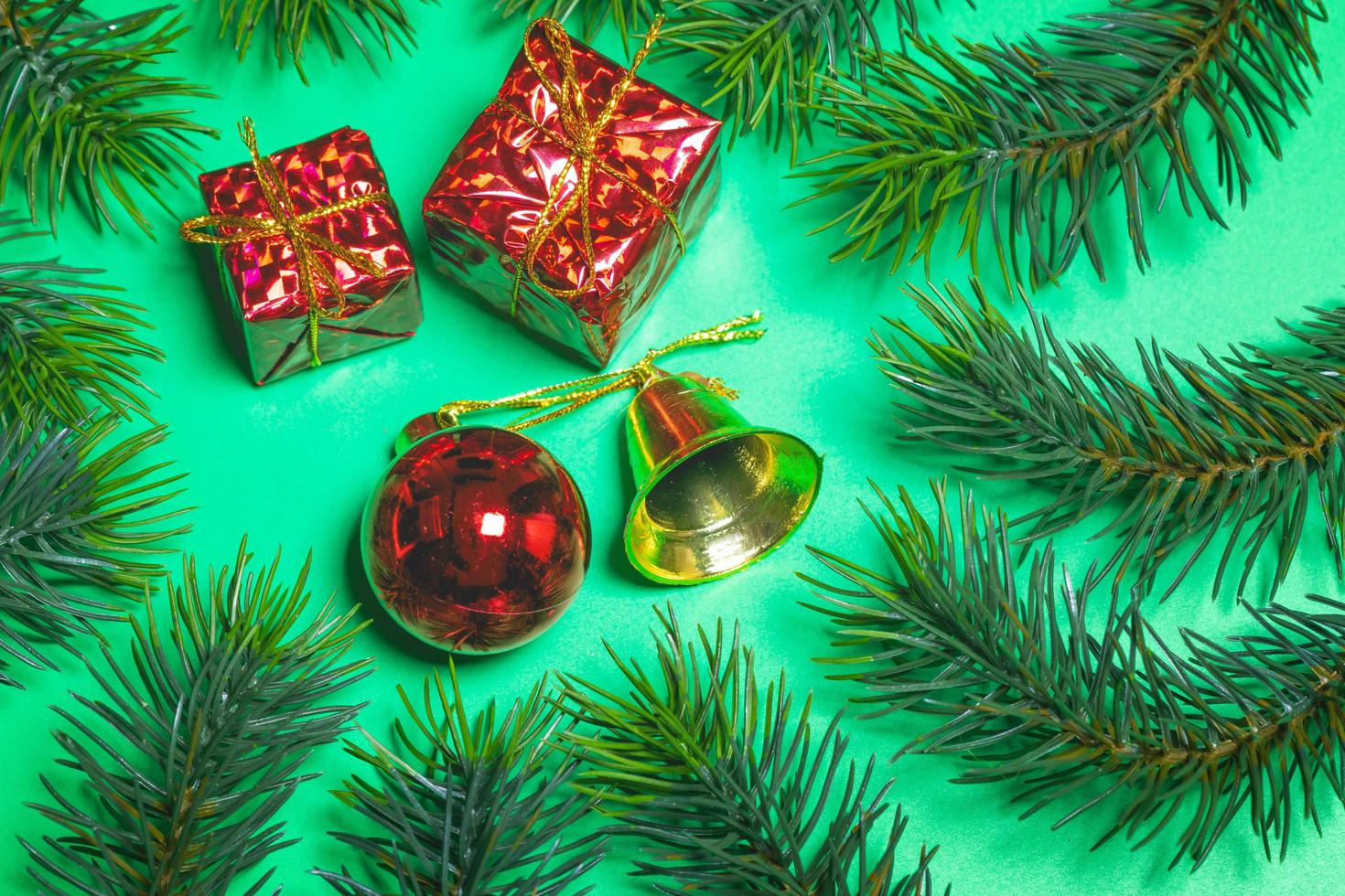 Top view of Christmas gift box red balls with spruce branches and bell on green background. photo