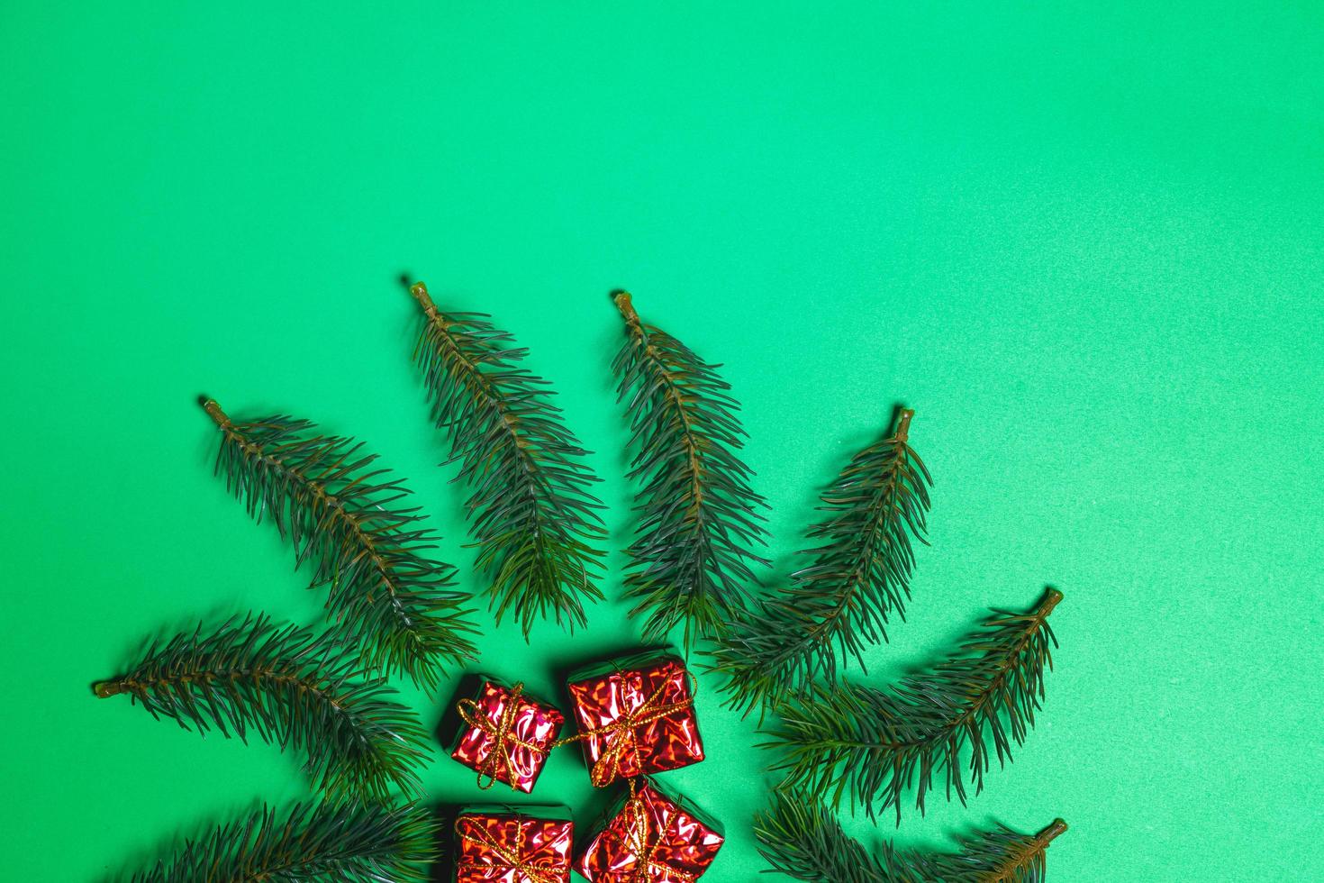Top view of Christmas gift box red balls with spruce branches and bell on green background. photo